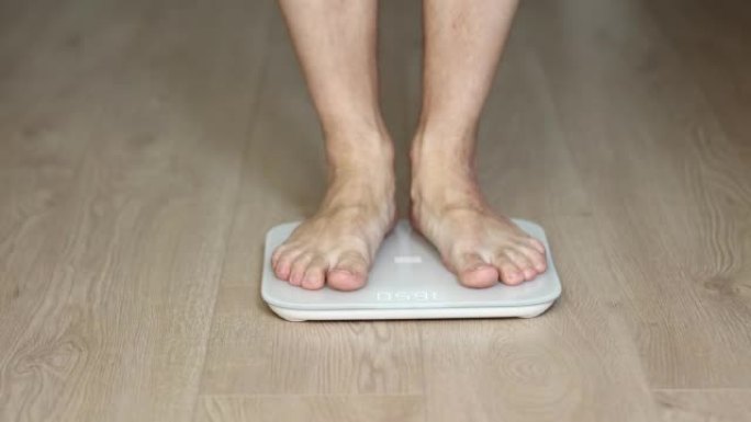 在秤上行走的人测量体重。男性沃尔检查BMI体重减轻。人体赤脚测量身体脂肪超重。男人的腿踩在浴室秤上