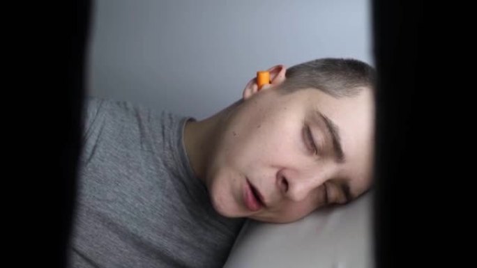 这个人戴上耳塞。橙色隔音屏障的特写。深度睡眠。耳鼻喉科医生建议橙色耳罩减少环境噪音。提高了对声音的敏
