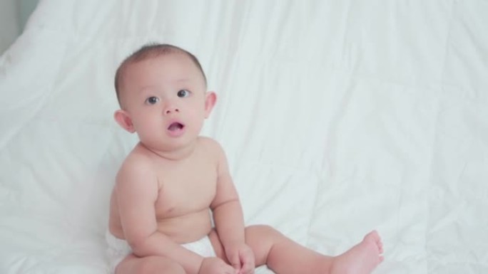 脸部可爱亚洲新生婴儿特写。在白色床上玩耍和爬行时，看着相机，笑容满面。天真的小新婴儿可爱。