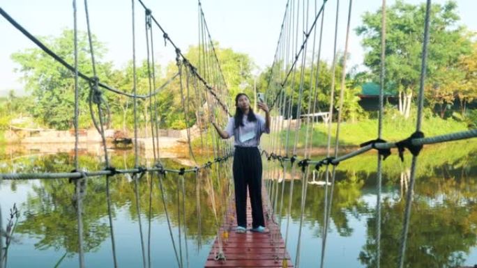 亚洲女孩在早晨的长袍桥或吊桥上通过智能手机自拍自己，生活方式概念。