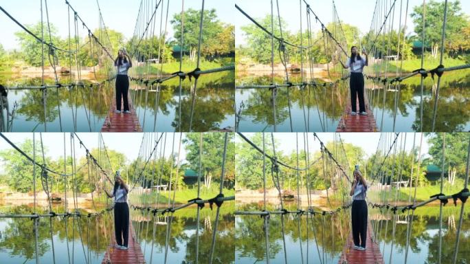 亚洲女孩在早晨的长袍桥或吊桥上通过智能手机自拍自己，生活方式概念。