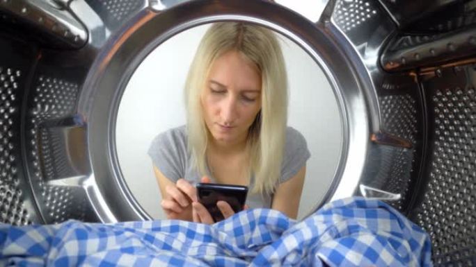一名妇女通过敞开的洗衣机门看着她的智能手机。