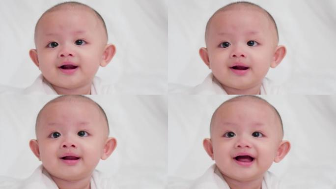 脸部特写可爱的亚洲新生婴儿躺在白色床上玩耍看着相机笑着开心的脸。天真的小新婴儿可爱。