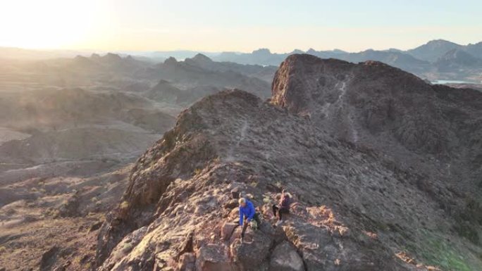 日出时成熟夫妇上升沙漠山脊的鸟瞰图