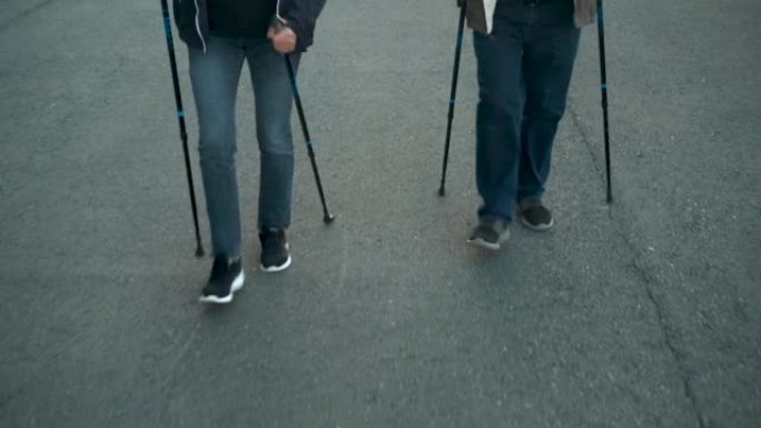 养老金领取者在公园里从事斯堪的纳维亚散步。一个男人和一个女人用棍子走路来改善健康。腿靠近。