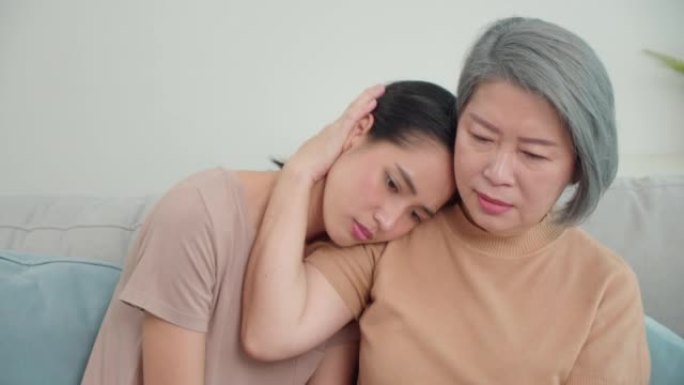 亚洲女儿与母亲坐在客厅沙发上感到压力和悲伤。女人的绝望和遗憾的情绪。