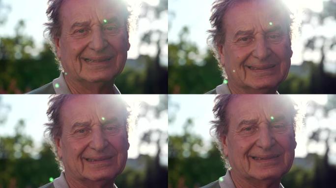 一位快乐的成熟老人肖像脸对着镜头微笑，站在户外，阳光照耀。公园里的70多岁男性