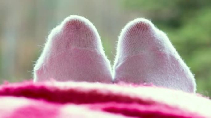 穿着白色袜子的脚，在山的酒店的阳台边缘盖着毯子的一半。度假旅行概念。女人在放松，在阳台上休息，在背景