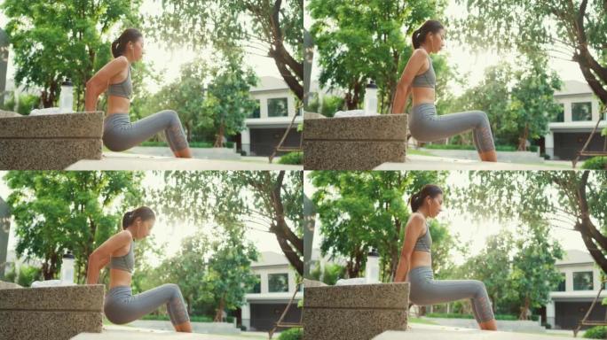 快乐的年轻运动型亚洲女性穿着带耳机的运动装，使用长凳使体重长凳三头肌浸入早晨在家庭花园公园锻炼。
