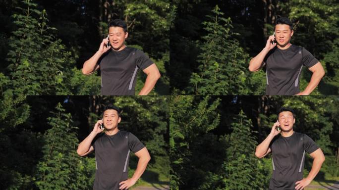 英俊的亚洲男人在手机上聊天站在阳光下微笑。男跑步者在外面健康锻炼健身。手机通话与朋友分享运动结果。慢