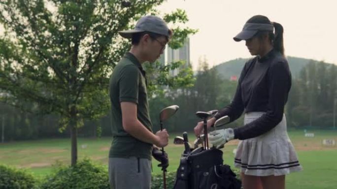亚洲女高尔夫球手从高尔夫球袋中选择司机高尔夫俱乐部，教男孩如何在高尔夫球场上打高尔夫球