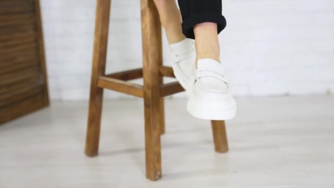 白色鞋子与普通的大鞋底展示。穿着现代鞋类的女士坐在桌子上挥舞着她的脚。特写。