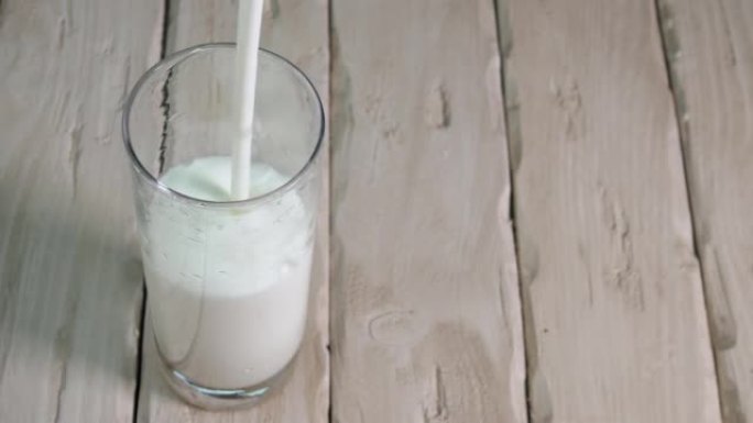 将酸奶倒入老式木板上的玻璃杯中。透明玻璃杯中的牛奶饮料