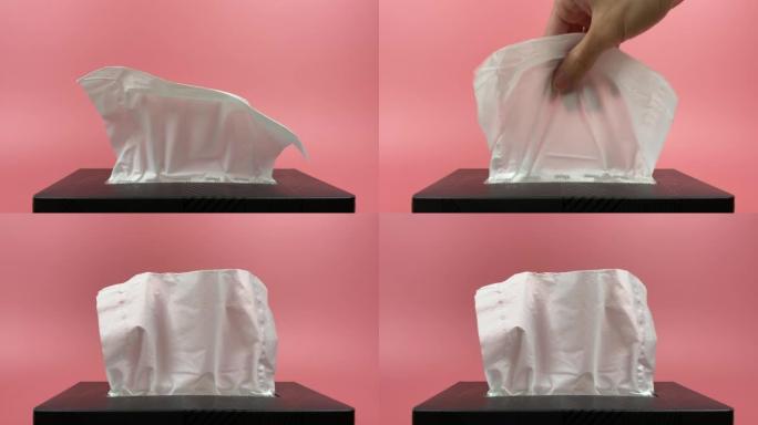 用手从分离在粉红色背景上的纸巾盒中拉出一块纸巾。