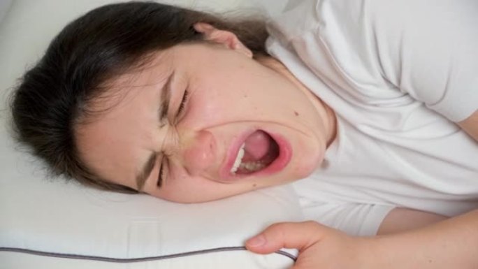 一名30岁的黑发女子躺在床上的枕头上打哈欠。
