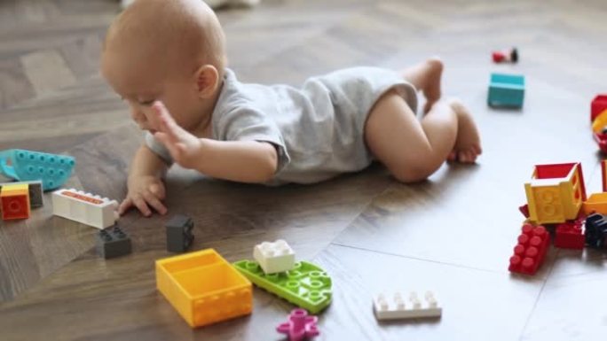 蹒跚学步的婴儿在地板客厅玩彩色砖块和橙色盒子