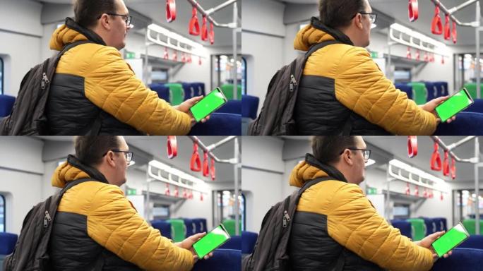 绿屏和火车在线浏览的man watch智能手机的背面视图。模拟观看手机上的内容。站在公共交通工具室内