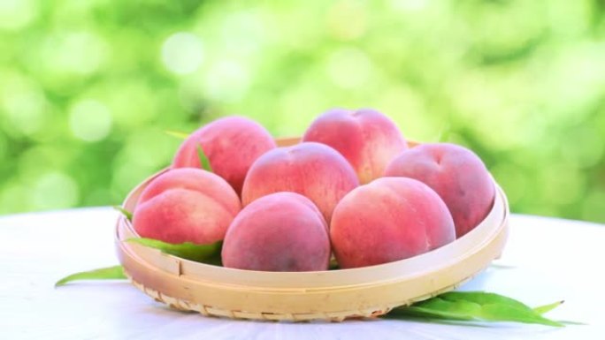 模糊花园背景中的粉红色和黄色桃子水果，花园木桌上的竹篮中的白色桃子。