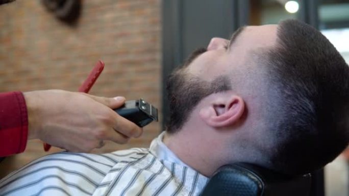 客户坐在理发店的椅子上，一边剪胡须。精英男士理发店