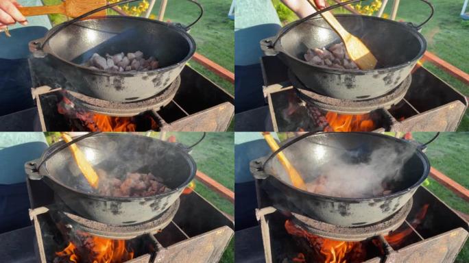 厨师用木铲在明火上的大锅中搅拌肉的手的特写镜头。