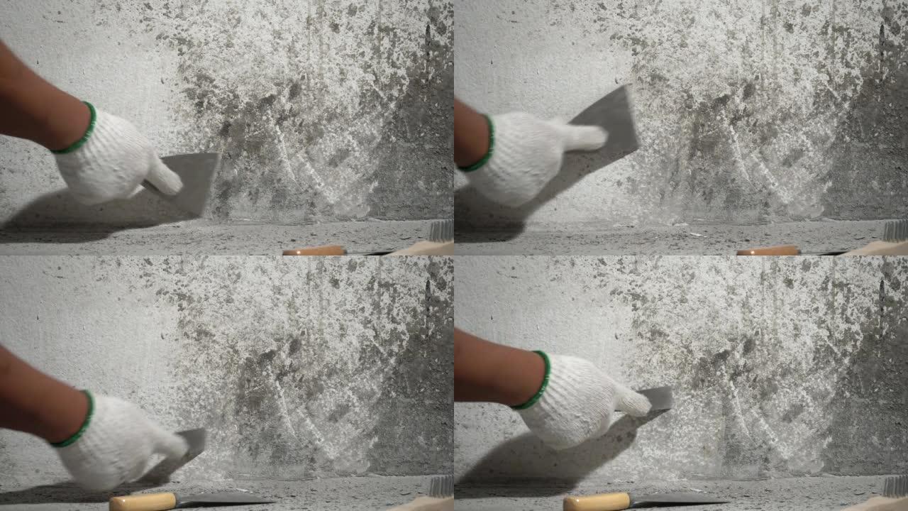 装修之家，画家从旧地板上飞溅的新混凝土层刮擦墙壁上的混凝土碎屑。