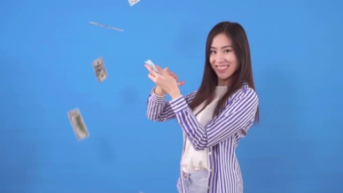 年轻美丽的亚洲女人散射纸钞美元站在蓝色背景慢莫