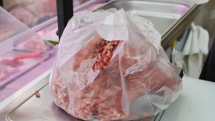 肉店店员的手的特写镜头，将碎肉放进一个站在秤上的袋子里。切碎的肉在商店的秤上称重，装在袋子里出售给买