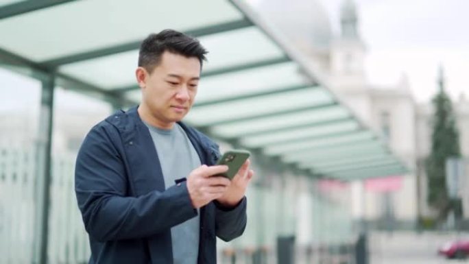 高级中国游客使用手机应用程序预订住宿和叫出租车，男子在机场附近带着行李箱。亚洲男子使用智能手机应用程