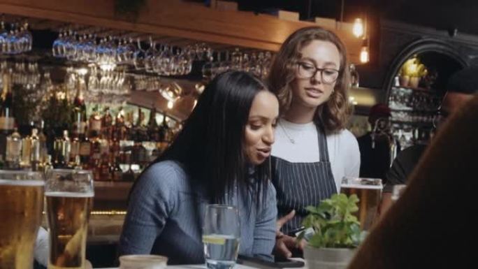 女服务员把打卡机带给餐厅的朋友。其中一名妇女通过在卡片机上轻按手机来支付晚餐费用。