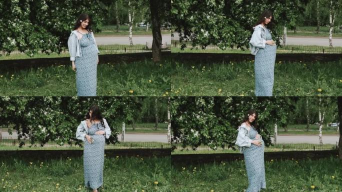 美丽快乐的怀孕黑发女人走在盛开的苹果园里。