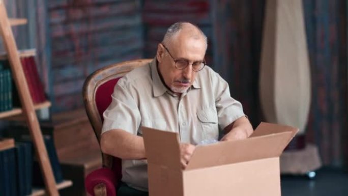 微笑成熟的70年代祖父打开包裹纸板箱网上商店订单送货乡村家居