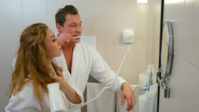 穿着浴袍的年轻夫妇在镜子前的浴室里一起清洁牙齿。
