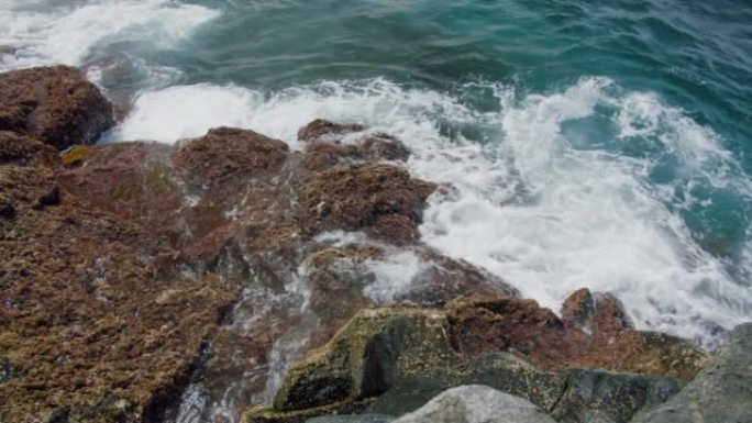 特写，海浪在特内里费岛海滩上的湿石头上冲刷，阳光照在发泡水中