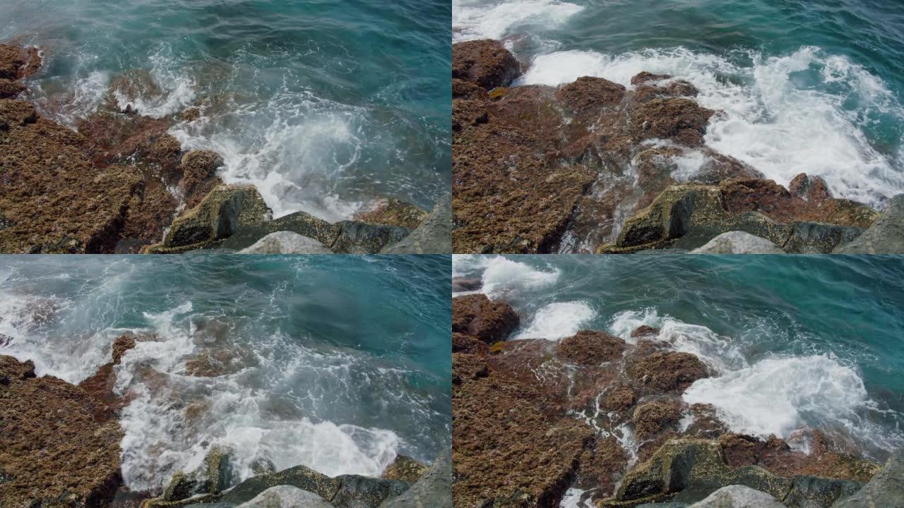 特写，海浪在特内里费岛海滩上的湿石头上冲刷，阳光照在发泡水中