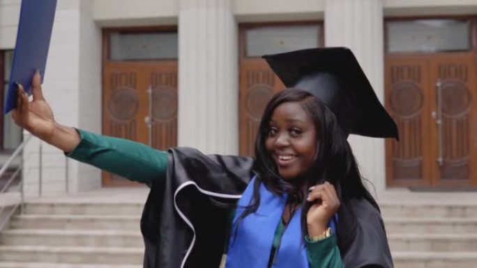 穿着黑色地幔的害羞的非裔美国女毕业生穿着地幔，拥有大学背景的研究生文凭。一个重要的事件。年轻专家