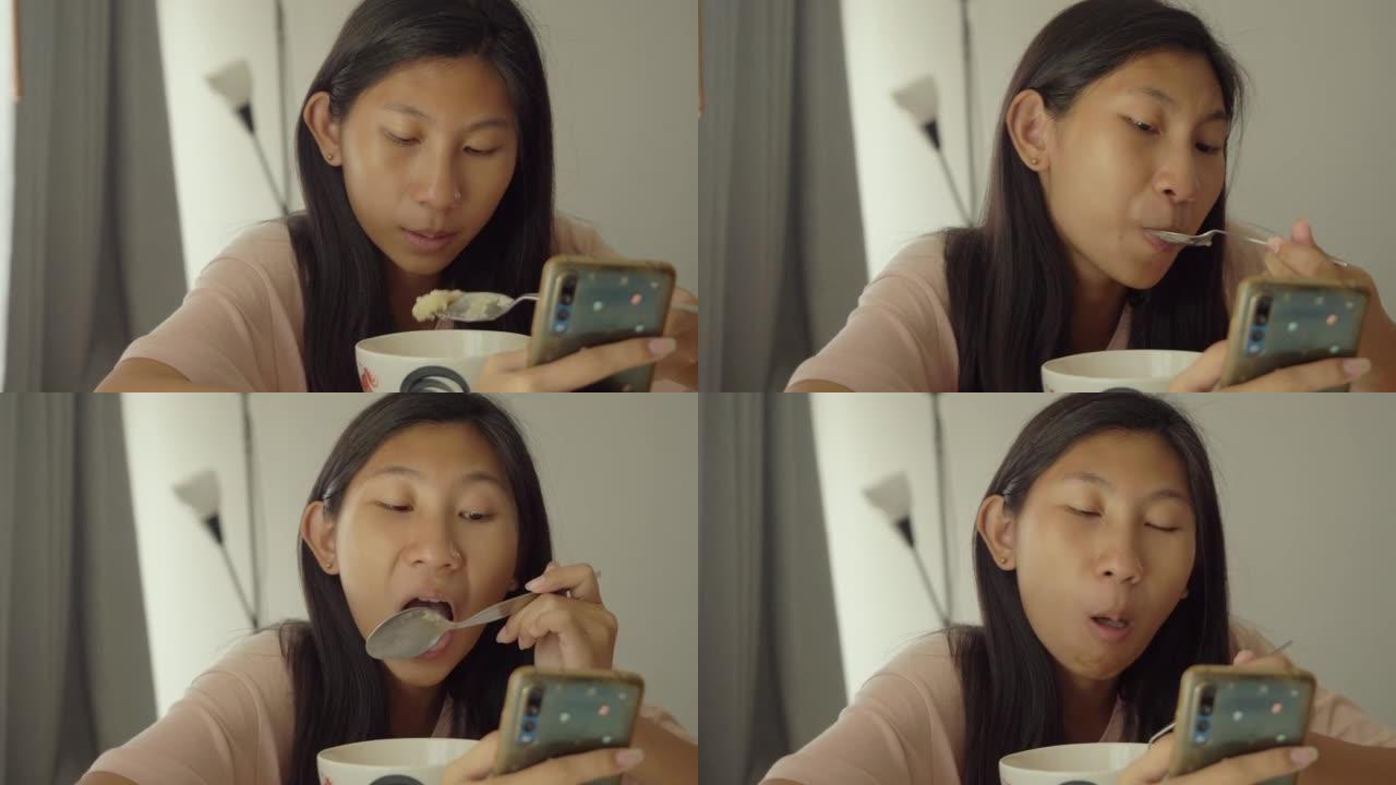 亚洲女孩在家里吃午餐时通过智能手机看电影或病毒视频，生活方式概念。