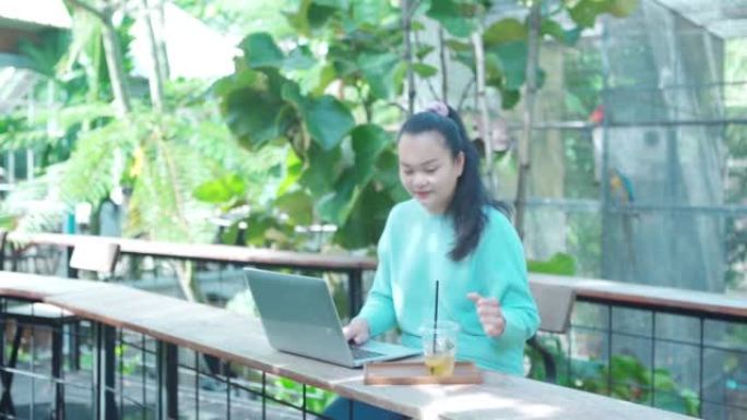 年轻的亚洲自由女性使用数字平板电脑在花园里在线工作，用稻草喝冰水