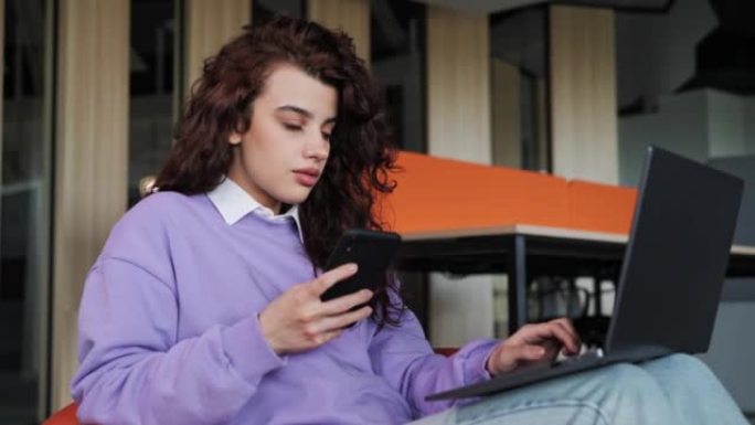 微笑的年轻女商人专业使用手机在笔记本电脑上工作坐在舒适的椅子上打字信息。女性顾客制作确认在线网站购物
