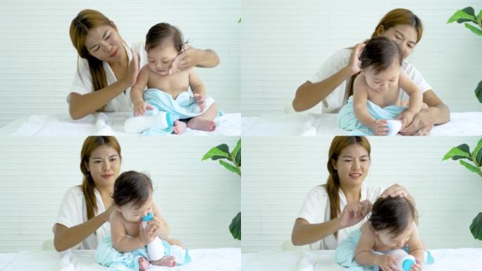 可爱的女婴在妈妈洗澡后在身上涂上爽身粉，妈妈在床上给她的小女儿涂上粉粉，梳理她的女婴的头发