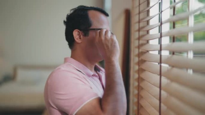悲伤的成熟印度男人透过他家的窗户看。