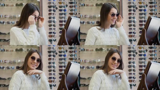 穿着舒适的白色毛衣的开朗年轻女子在光学沙龙的老式台镜附近试戴太阳镜，然后看着相机