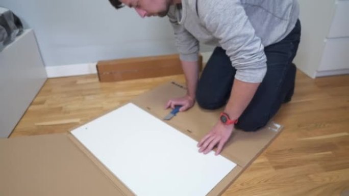买家在家里打开白色的桌子组装在一个纸板箱的地板上。一个男人买了家具，打开盒子。搬迁后的白色新家具。新