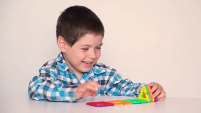 一个学龄前男孩兴高采烈地与磁性建造者玩耍，在白色背景上笑着说话