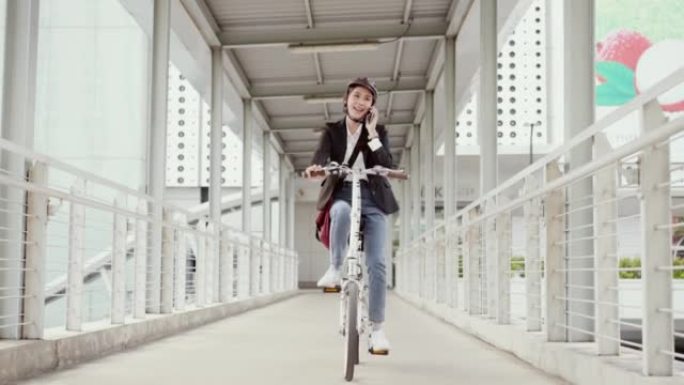 亚洲美丽的女商人戴着自行车头盔，骑着自行车穿过天桥到市中心的办公室上班。她只用一只手骑自行车时正在使