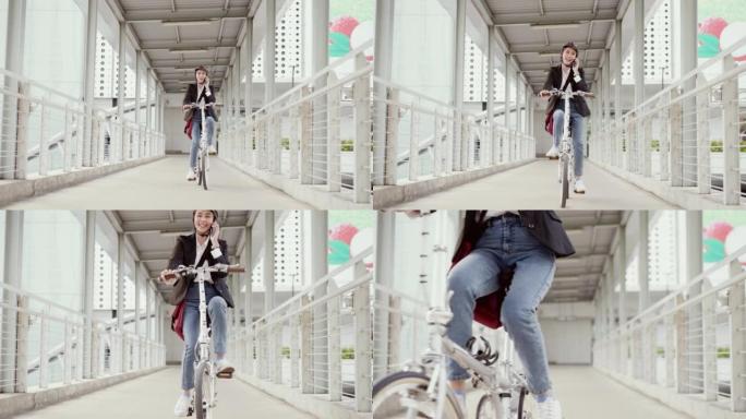 亚洲美丽的女商人戴着自行车头盔，骑着自行车穿过天桥到市中心的办公室上班。她只用一只手骑自行车时正在使