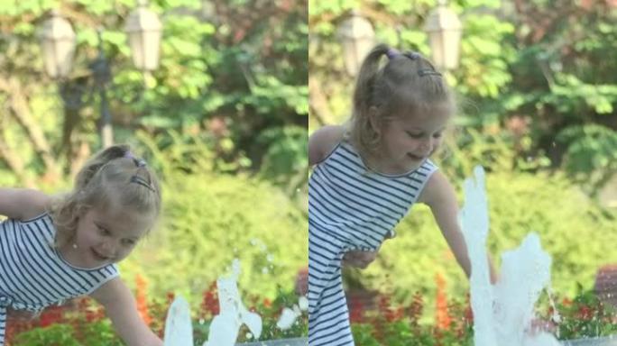 垂直视频: 妈妈的双手抱着微笑的小女儿在喷泉中嬉水。妈妈和小女孩在公园的喷泉里玩耍，微笑着。慢动作。