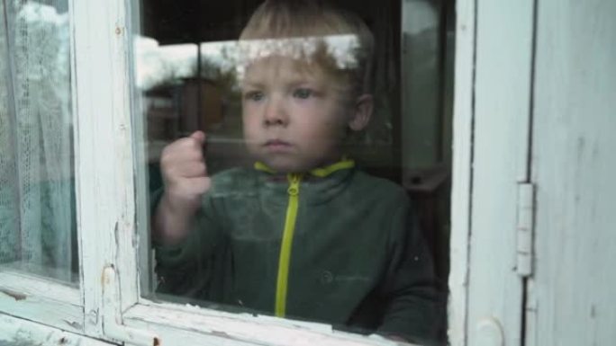 一个孤独的孤儿男孩透过一扇旧窗户看。