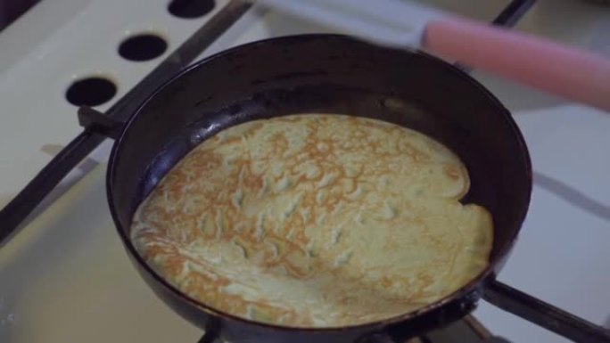 在黑色煎锅中烹饪煎饼的过程，在油炸过程中，用硅胶刮刀将煎饼翻转