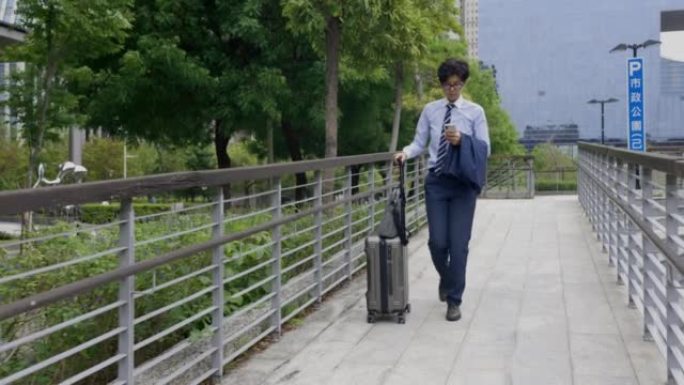 带着拉杆包的步行女商人看着她的智能手机