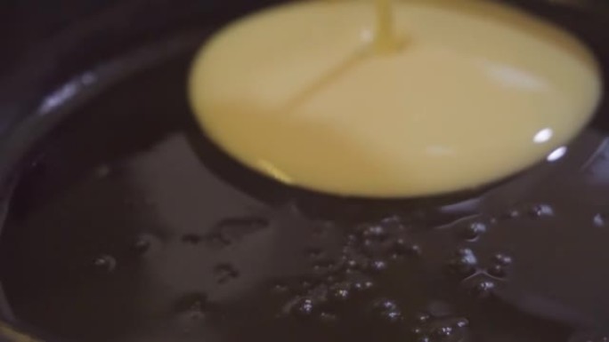 用液体面团制作煎饼的过程。用植物油润滑的黑锅，将面团倒在上面